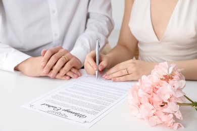 Photo of Newlyweds signing marriage contract at desk, closeup