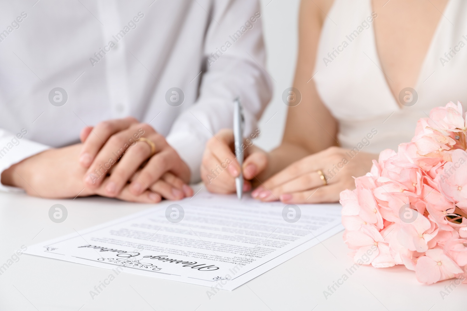 Photo of Newlyweds signing marriage contract at desk, closeup