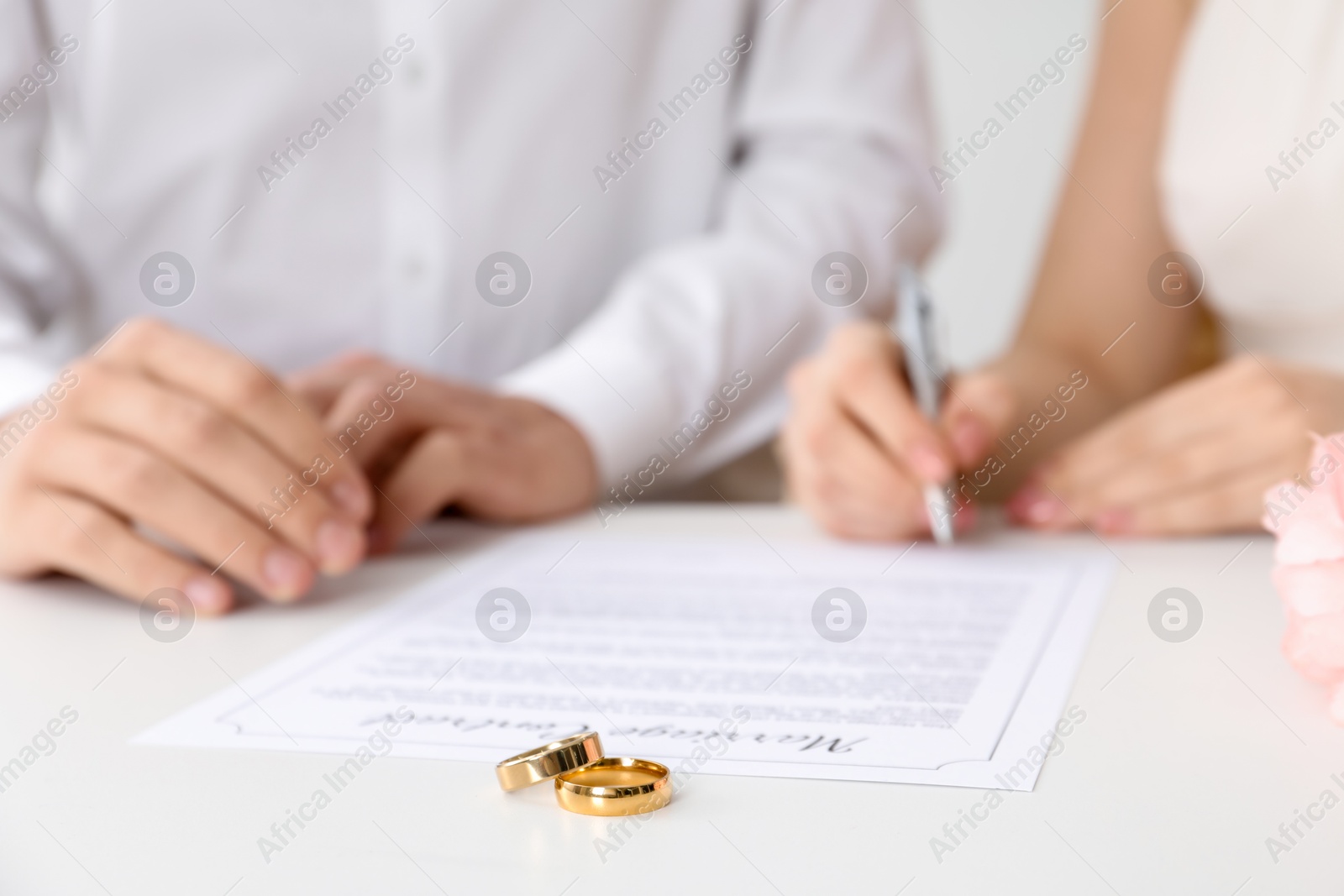 Photo of Newlyweds signing marriage contract and wedding rings on desk, selective focus