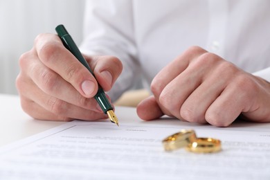 Photo of Man signing marriage contract and wedding rings on desk, selective focus