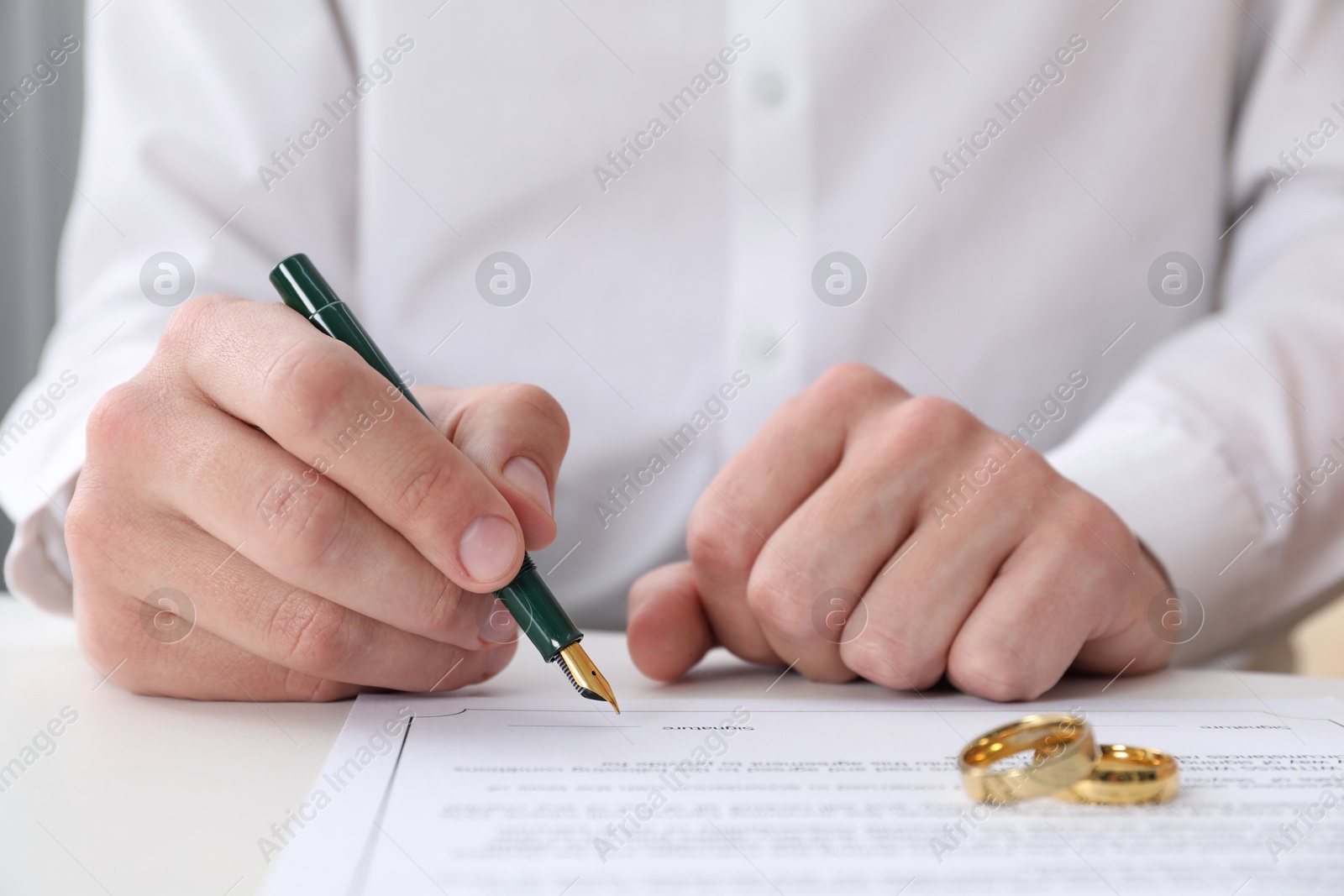 Photo of Man signing marriage contract and wedding rings on desk, closeup