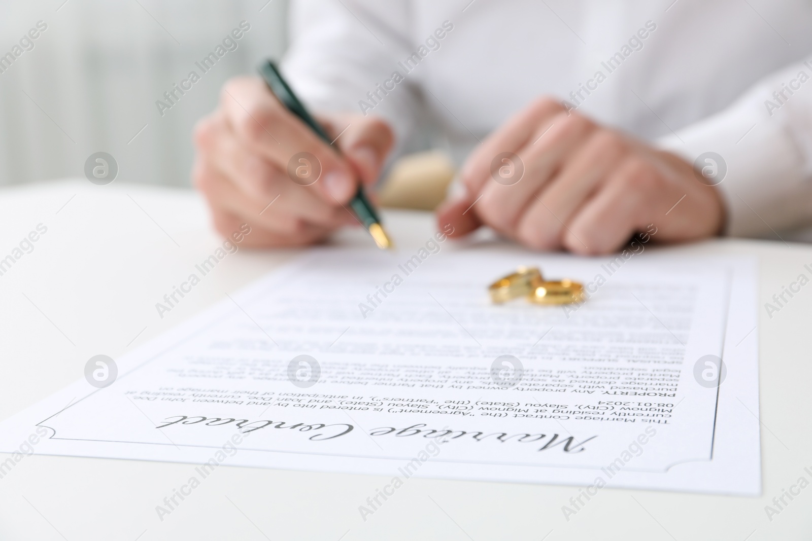 Photo of Man signing marriage contract and wedding rings on desk, selective focus