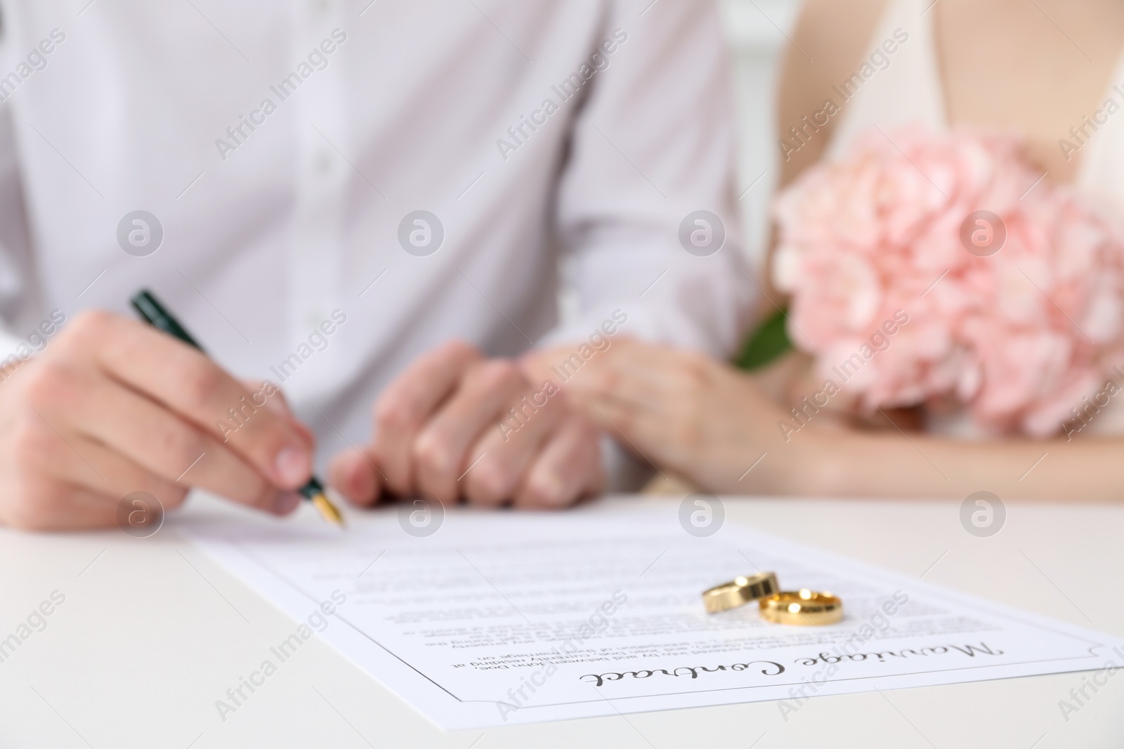 Photo of Newlyweds signing marriage contract and wedding rings on desk, selective focus