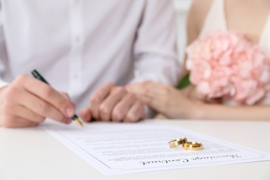 Photo of Newlyweds signing marriage contract and wedding rings on desk, selective focus