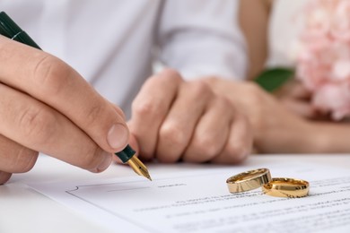 Photo of Newlyweds signing marriage contract and wedding rings on desk, selective focus