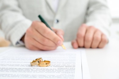 Photo of Man signing marriage contract and wedding rings on desk, selective focus