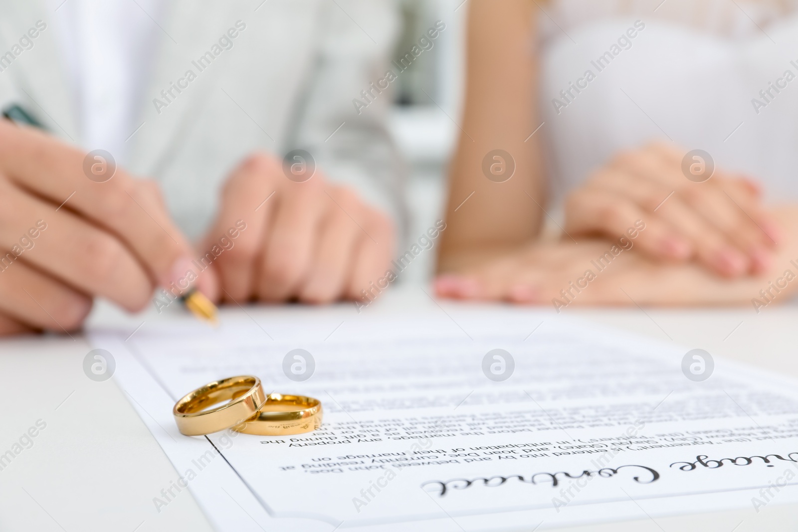 Photo of Newlyweds signing marriage contract and wedding rings on desk, selective focus