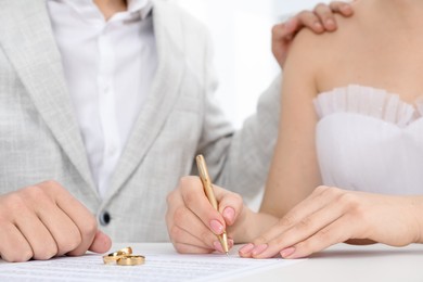 Photo of Newlyweds signing marriage contract and wedding rings on desk, selective focus