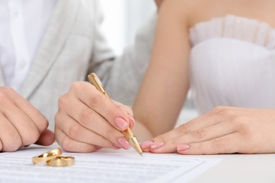 Photo of Newlyweds signing marriage contract and wedding rings on desk, selective focus