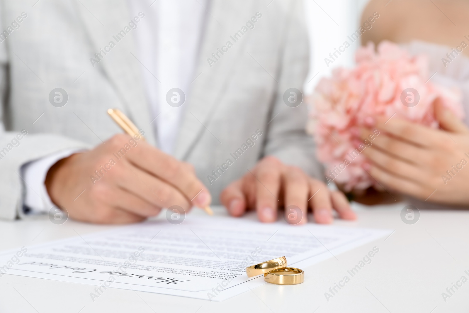 Photo of Newlyweds signing marriage contract and wedding rings on desk, selective focus