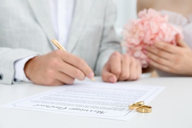 Photo of Newlyweds signing marriage contract and wedding rings on desk, selective focus