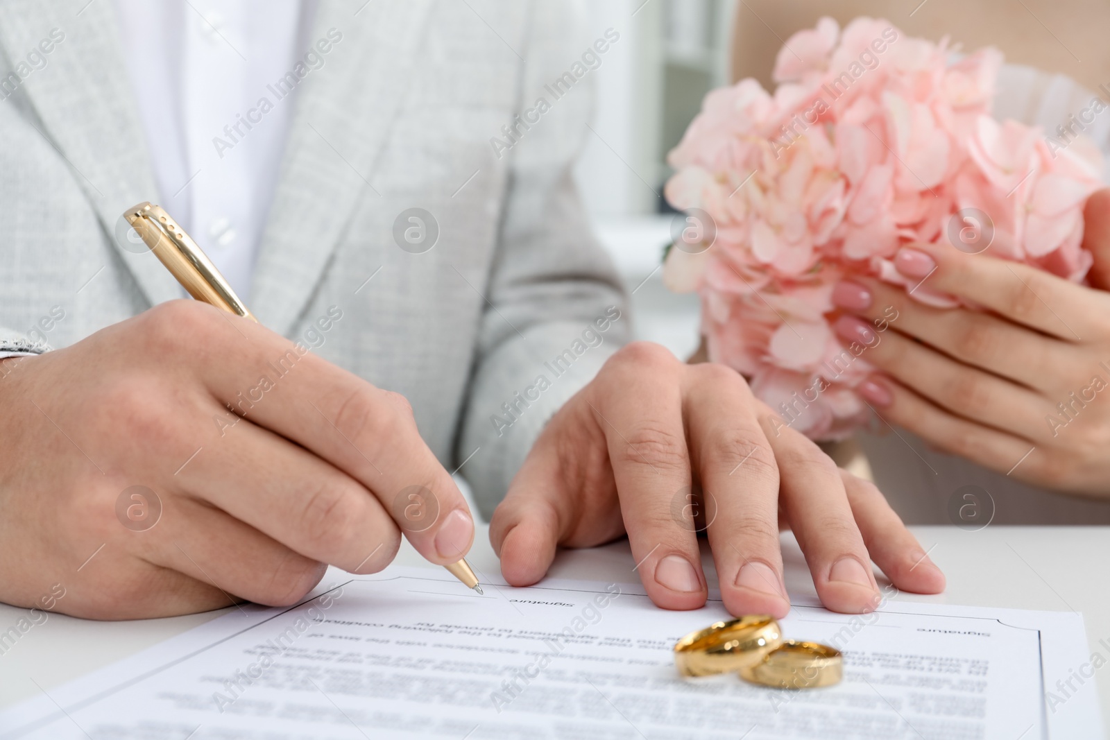 Photo of Newlyweds signing marriage contract and wedding rings on desk, selective focus