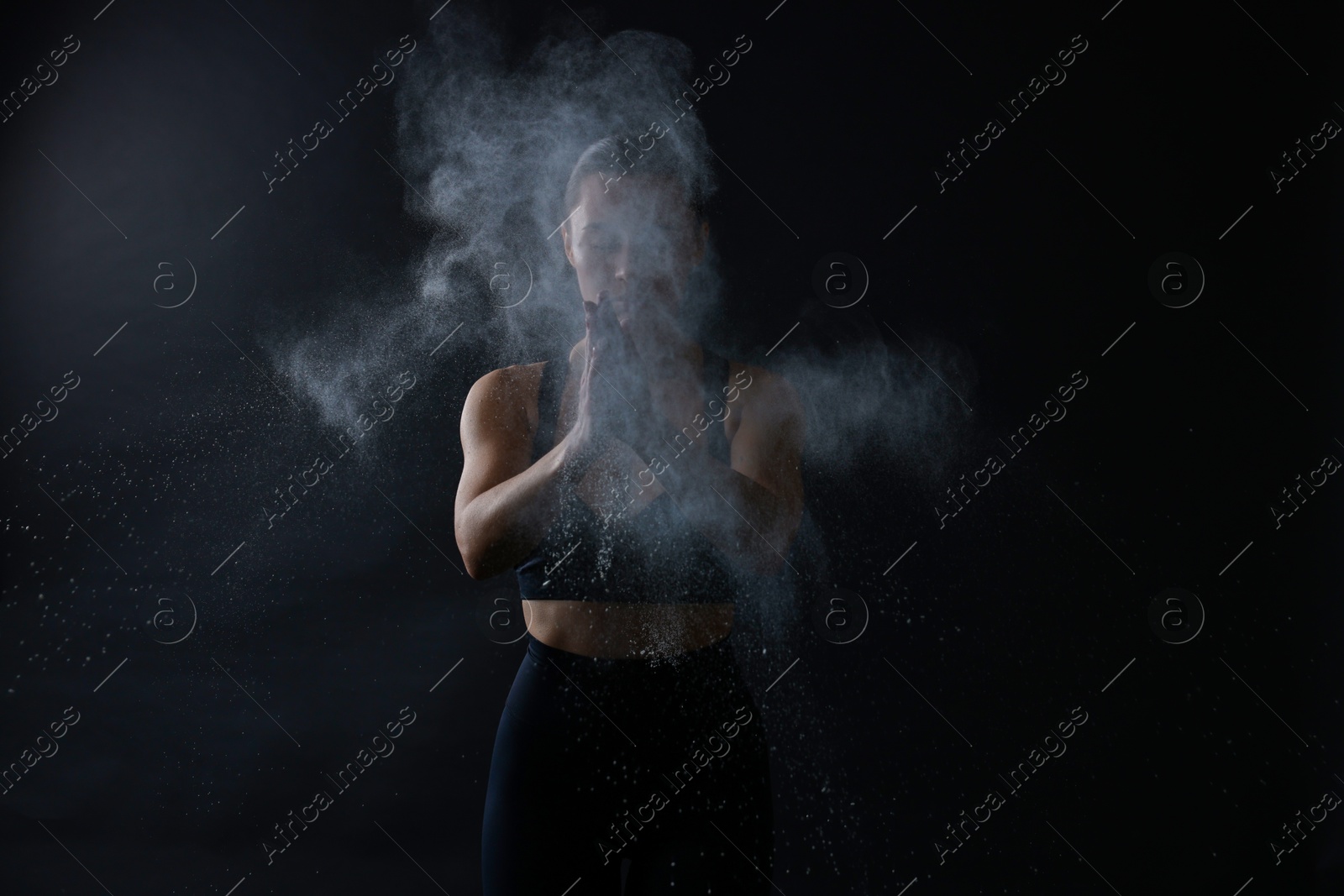 Photo of Woman clapping hands with talcum powder before training on black background