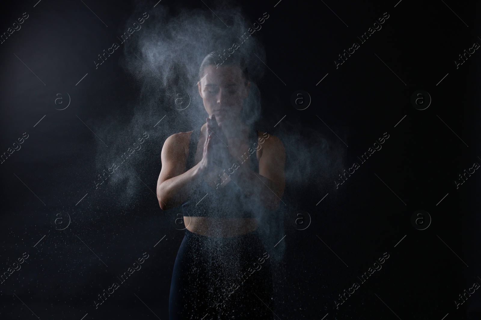 Photo of Woman clapping hands with talcum powder before training on black background