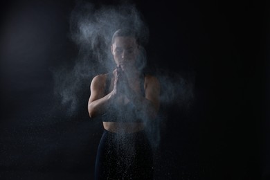 Photo of Woman clapping hands with talcum powder before training on black background