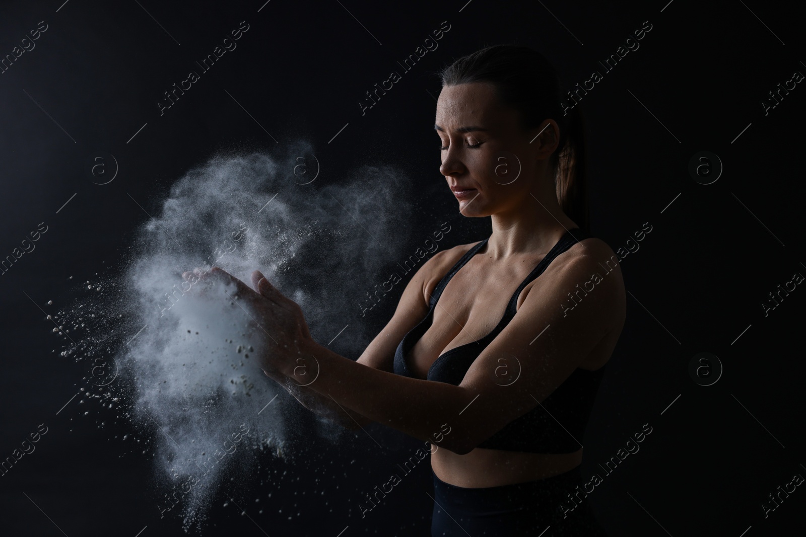 Photo of Woman clapping hands with talcum powder before training on black background