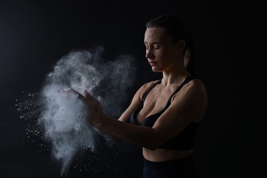 Photo of Woman clapping hands with talcum powder before training on black background