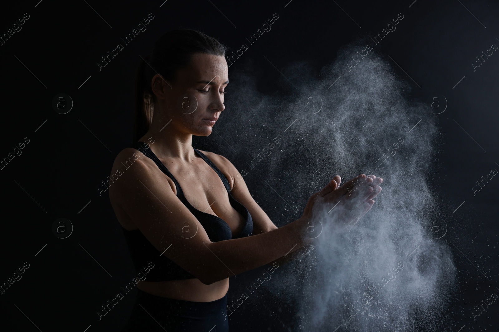 Photo of Woman clapping hands with talcum powder before training on black background