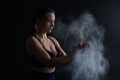 Photo of Woman clapping hands with talcum powder before training on black background