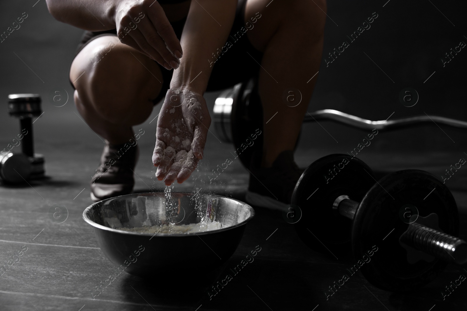 Photo of Woman applying talcum powder onto her hands above bowl before training in gym, closeup