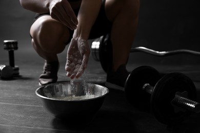 Photo of Woman applying talcum powder onto her hands above bowl before training in gym, closeup