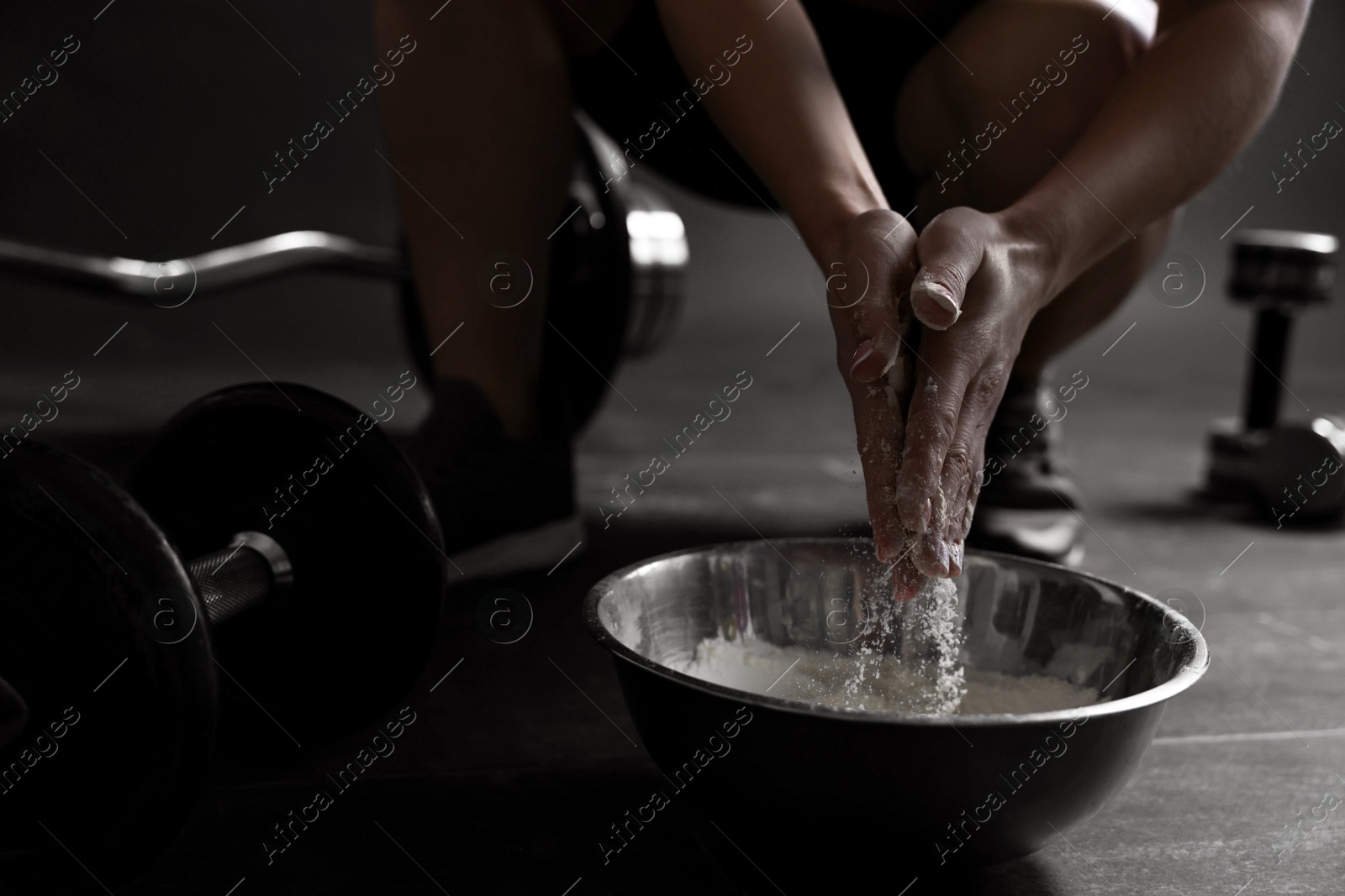 Photo of Woman applying talcum powder onto her hands above bowl before training in gym, closeup