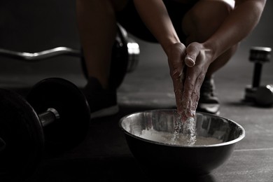 Photo of Woman applying talcum powder onto her hands above bowl before training in gym, closeup