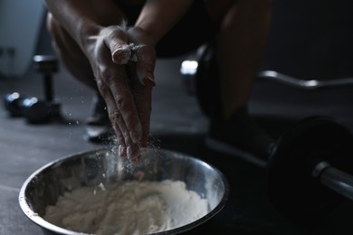 Photo of Woman applying talcum powder onto her hands above bowl before training in gym, closeup