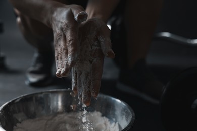 Photo of Woman applying talcum powder onto her hands above bowl before training in gym, closeup