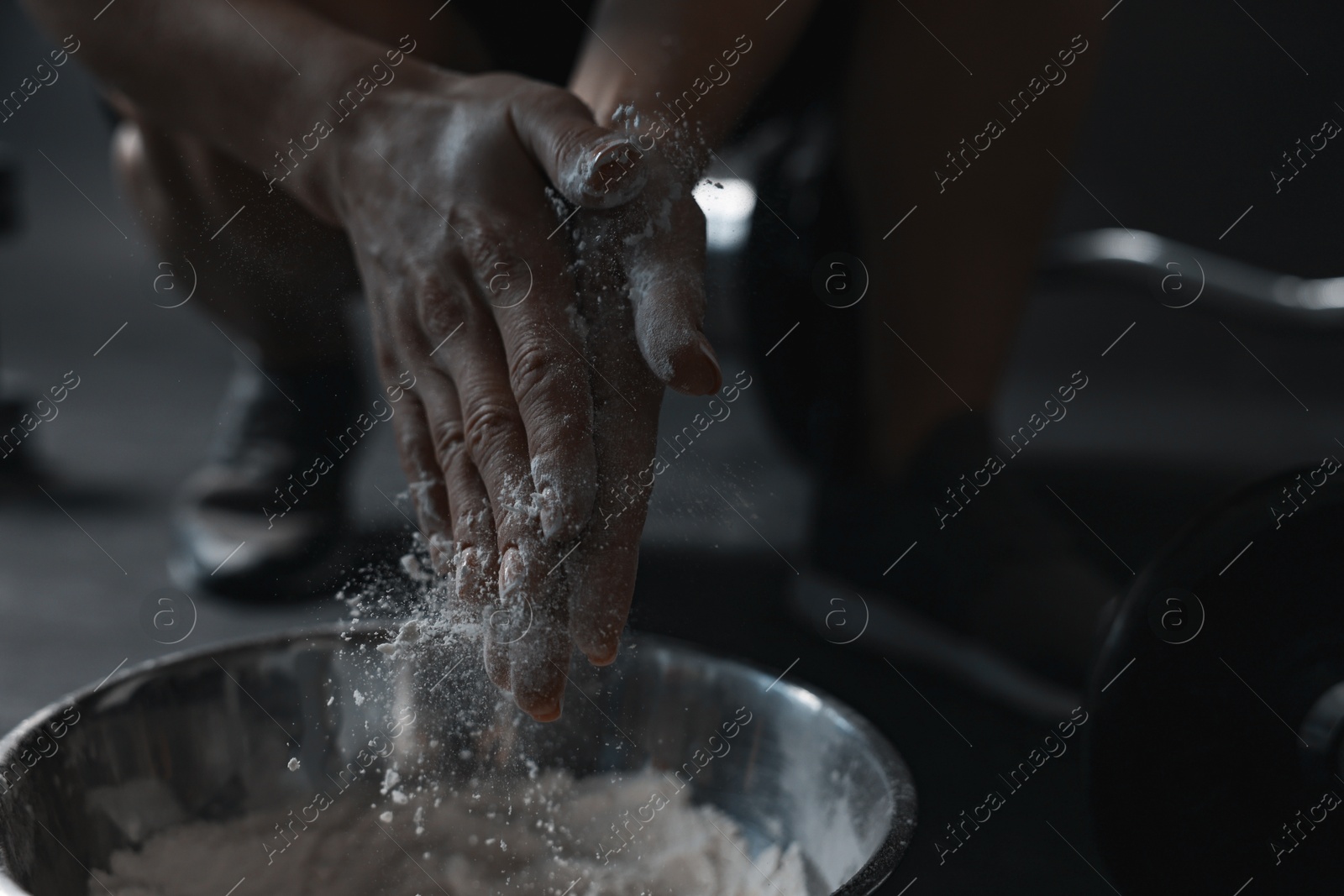 Photo of Woman applying talcum powder onto her hands above bowl before training in gym, closeup