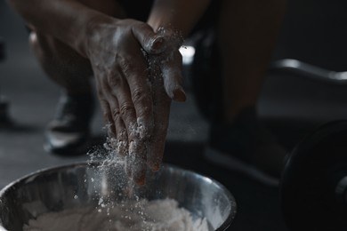 Photo of Woman applying talcum powder onto her hands above bowl before training in gym, closeup