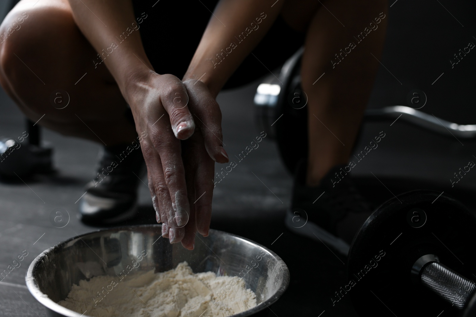 Photo of Woman applying talcum powder onto her hands above bowl before training in gym, closeup