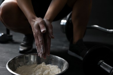 Photo of Woman applying talcum powder onto her hands above bowl before training in gym, closeup