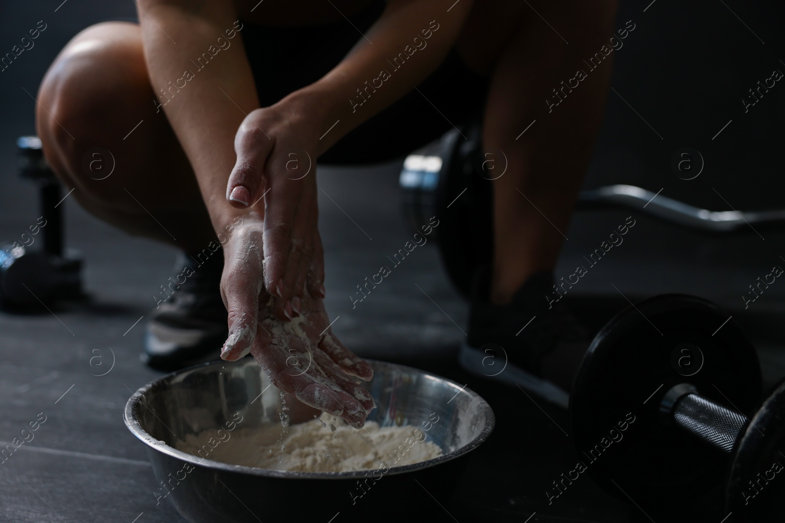 Photo of Woman applying talcum powder onto her hands above bowl before training in gym, closeup