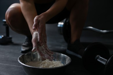 Photo of Woman applying talcum powder onto her hands above bowl before training in gym, closeup