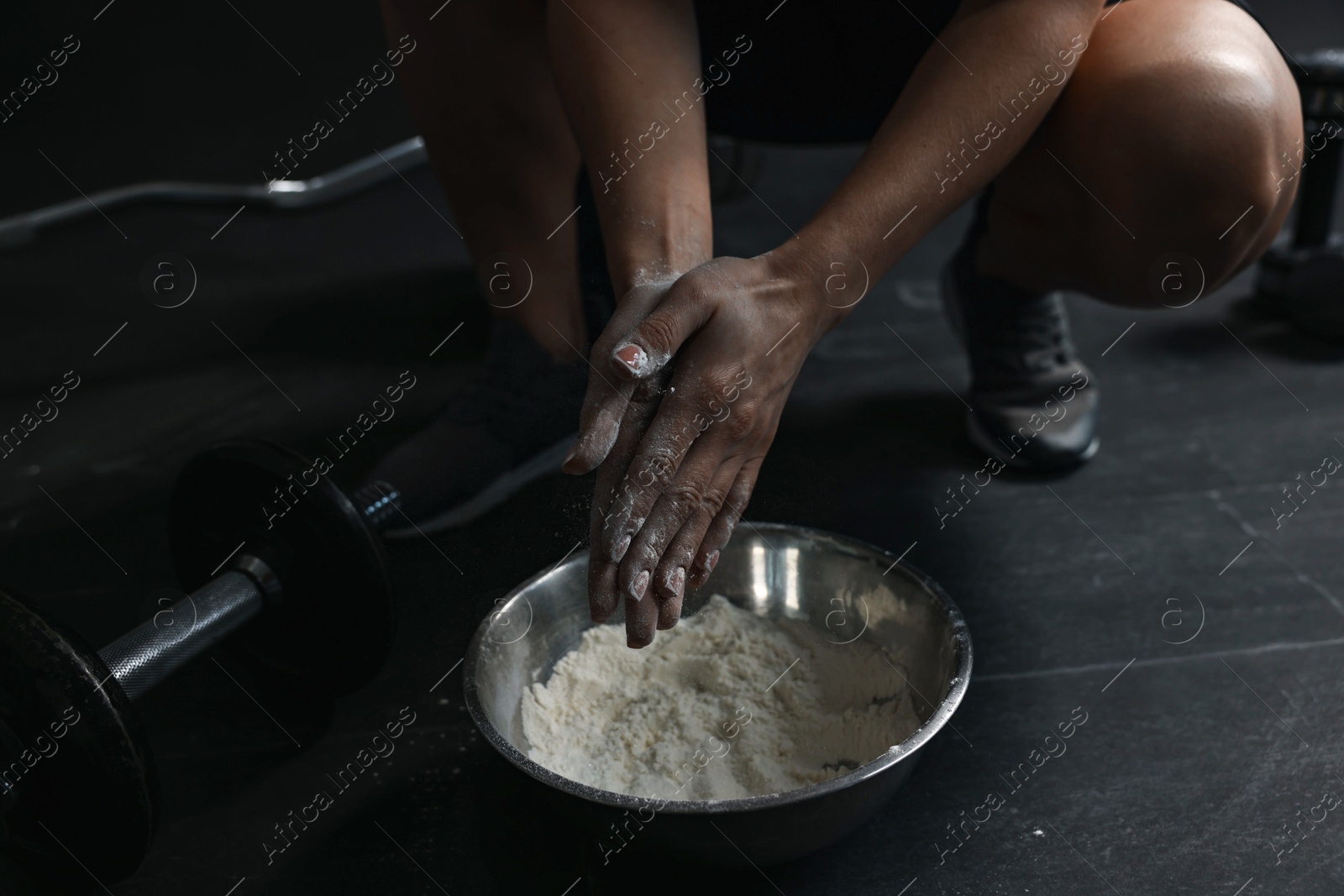 Photo of Woman applying talcum powder onto her hands above bowl before training in gym, closeup