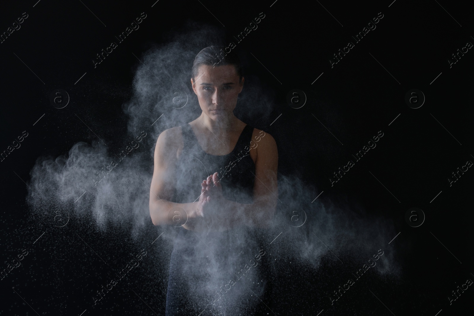 Photo of Woman clapping hands with talcum powder before training on black background