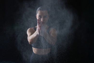 Photo of Woman clapping hands with talcum powder before training on black background