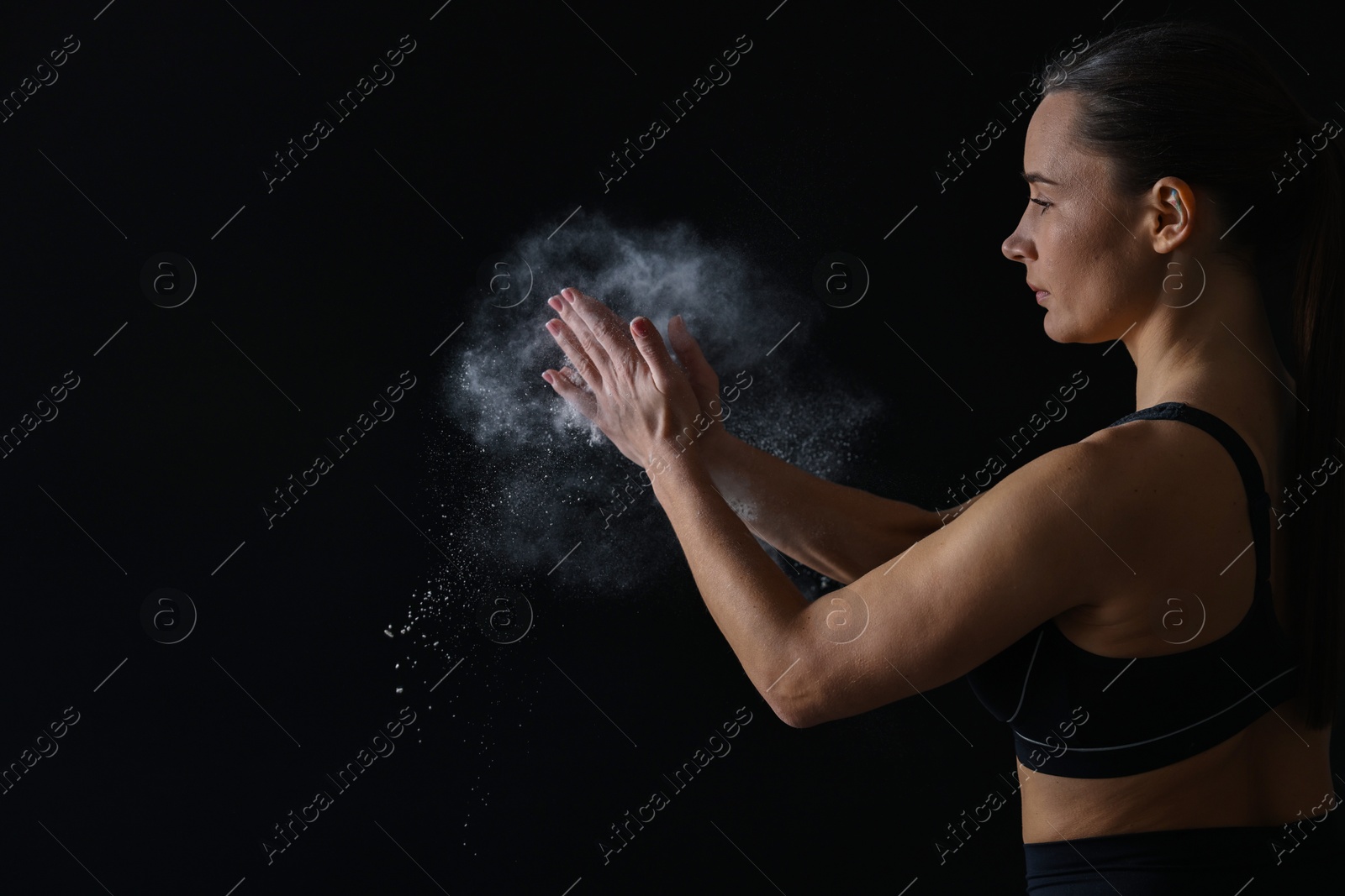 Photo of Woman clapping hands with talcum powder before training on black background, space for text