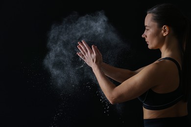 Woman clapping hands with talcum powder before training on black background, space for text