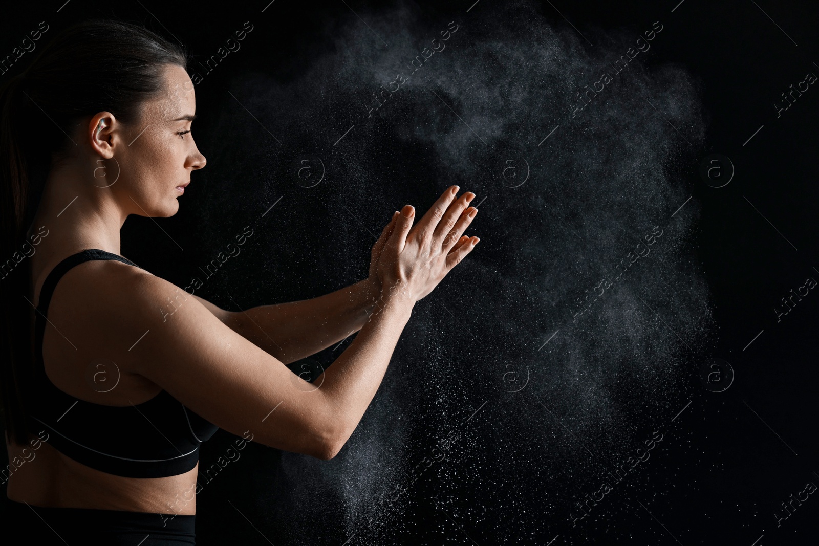 Photo of Woman clapping hands with talcum powder before training on black background, space for text