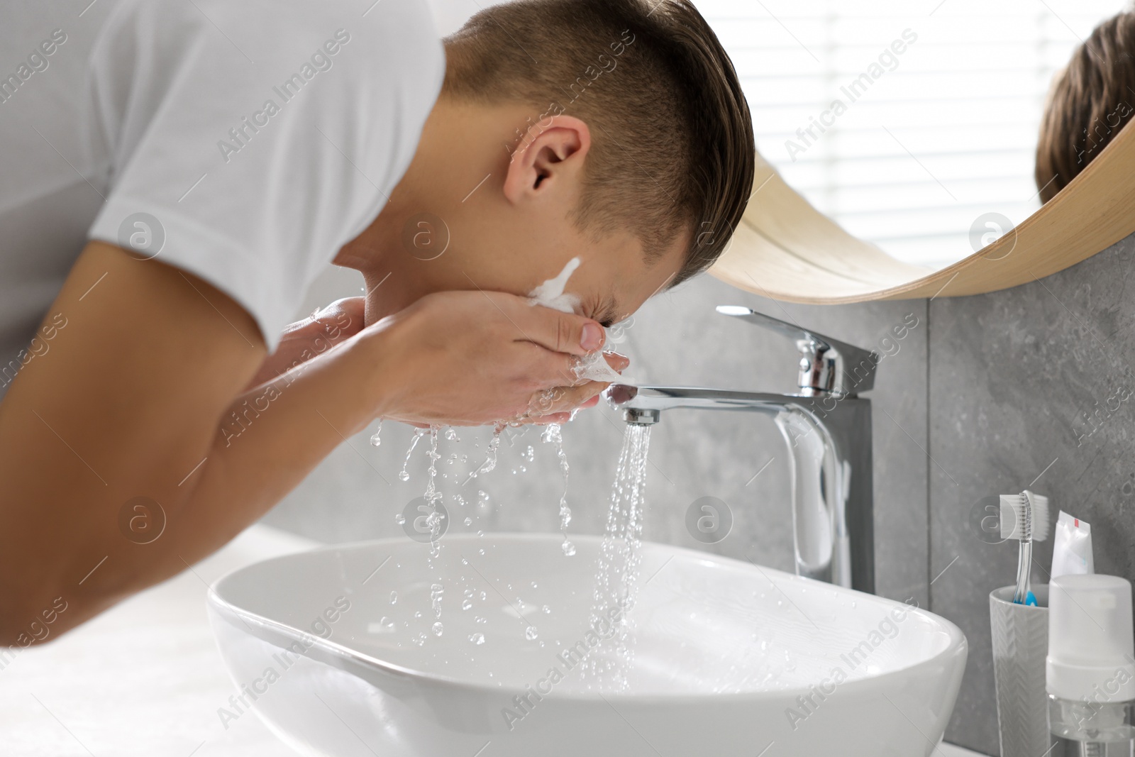 Photo of Man washing his face with cosmetic product over sink in bathroom