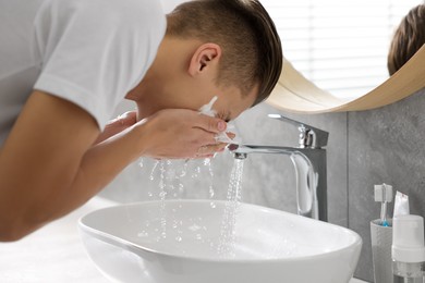 Photo of Man washing his face with cosmetic product over sink in bathroom