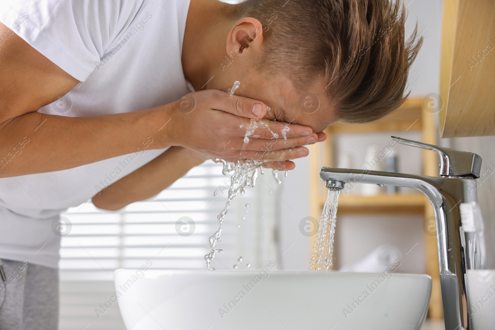 Photo of Man washing his face over sink in bathroom