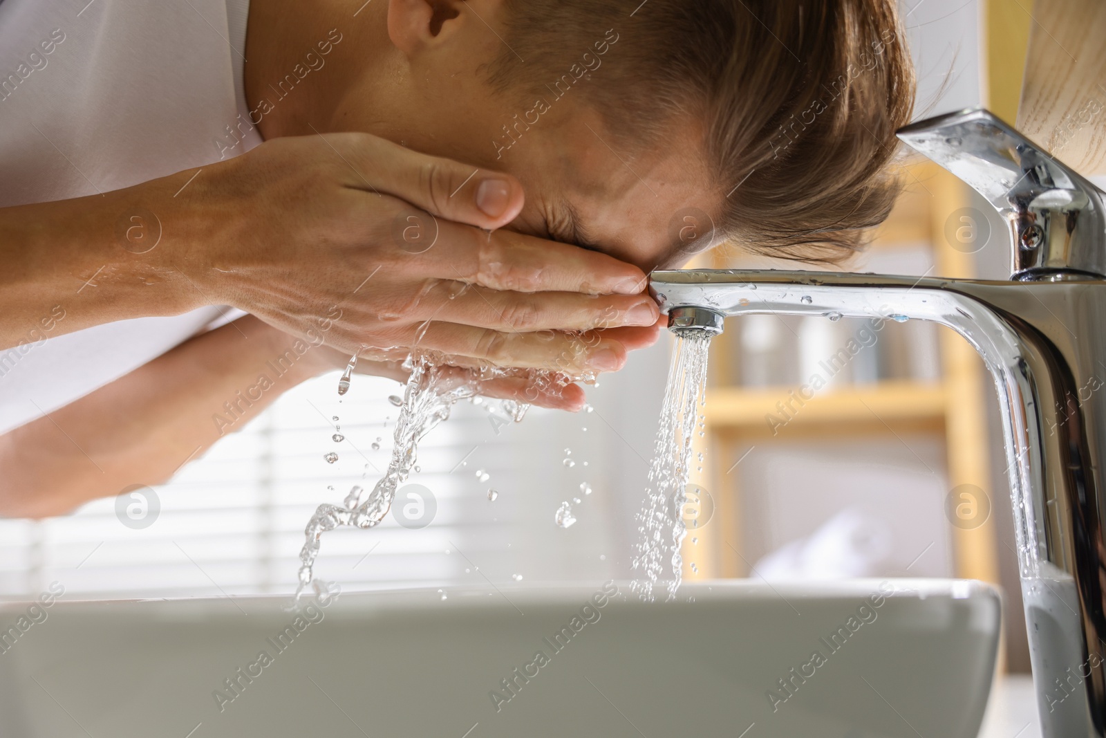 Photo of Man washing his face over sink in bathroom