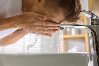 Photo of Man washing his face over sink in bathroom