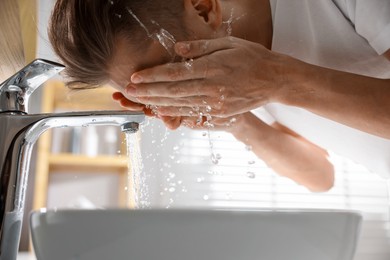 Photo of Man washing his face over sink in bathroom