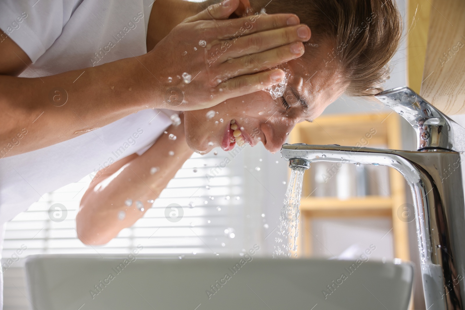 Photo of Man washing his face over sink in bathroom