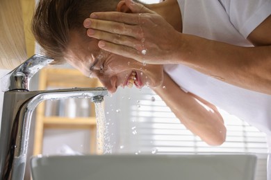 Photo of Man washing his face over sink in bathroom