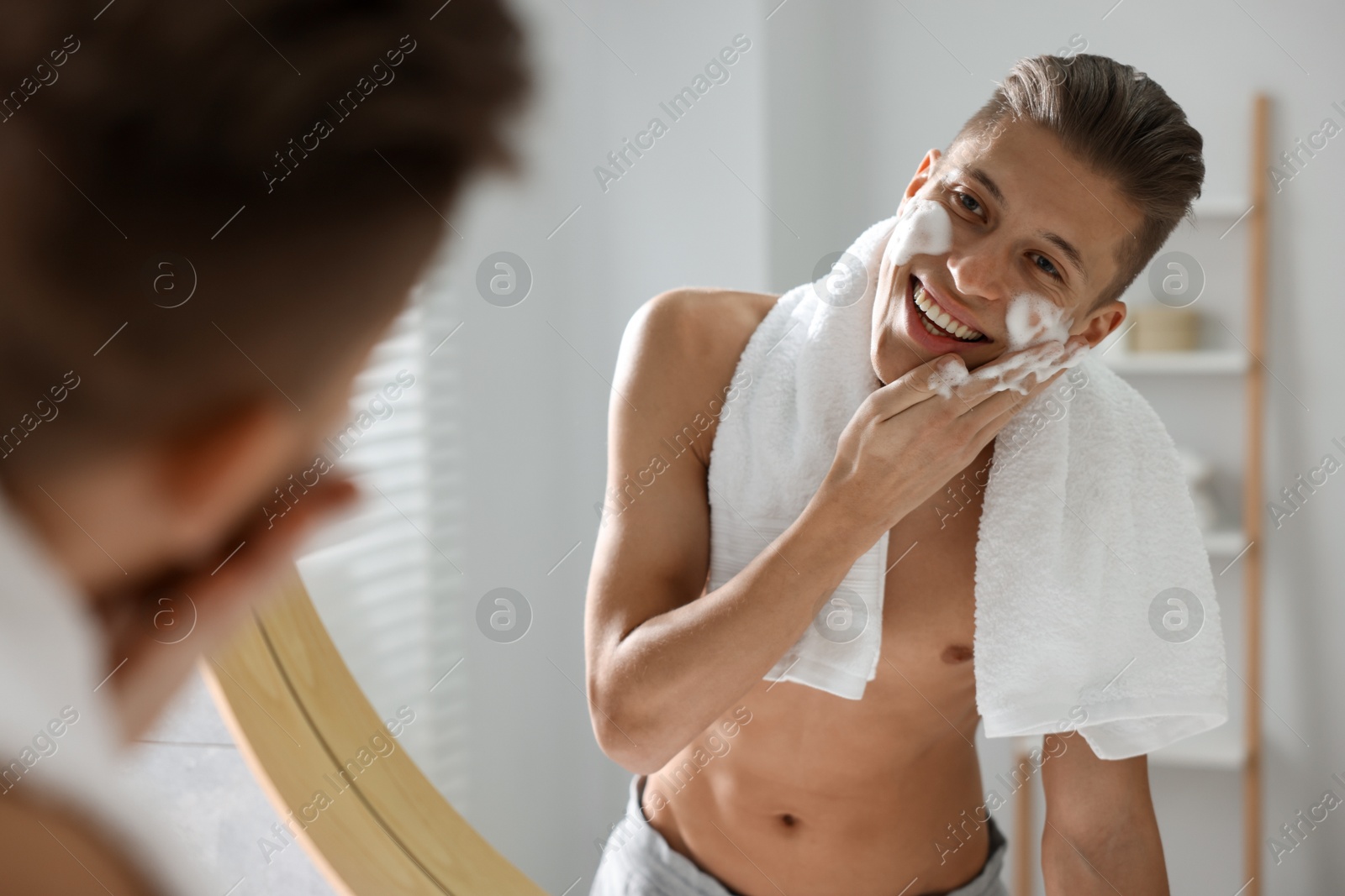 Photo of Man washing his face with cosmetic product near mirror in bathroom